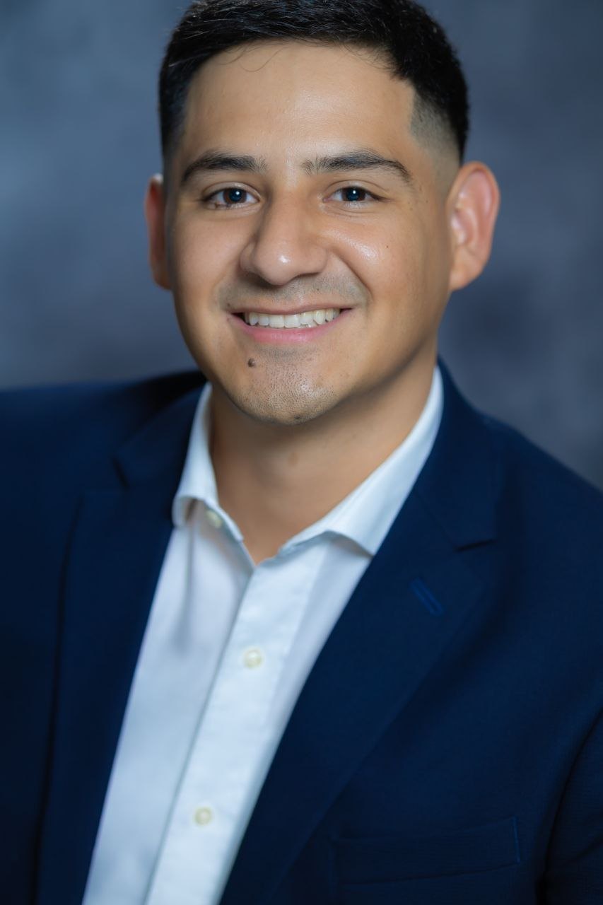 Kevin Lucano, smiling, in a navy suit against a grey studio backdrop.